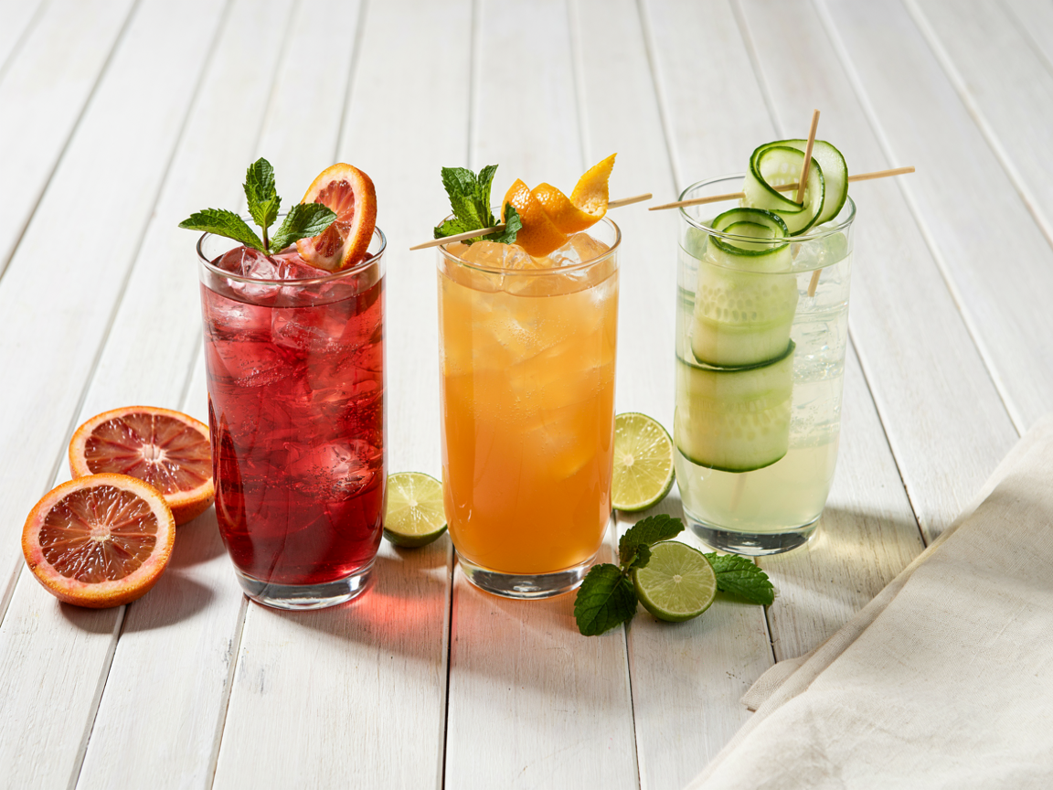 Three colorful sugar-free mocktails in tall glasses with citrus and mint