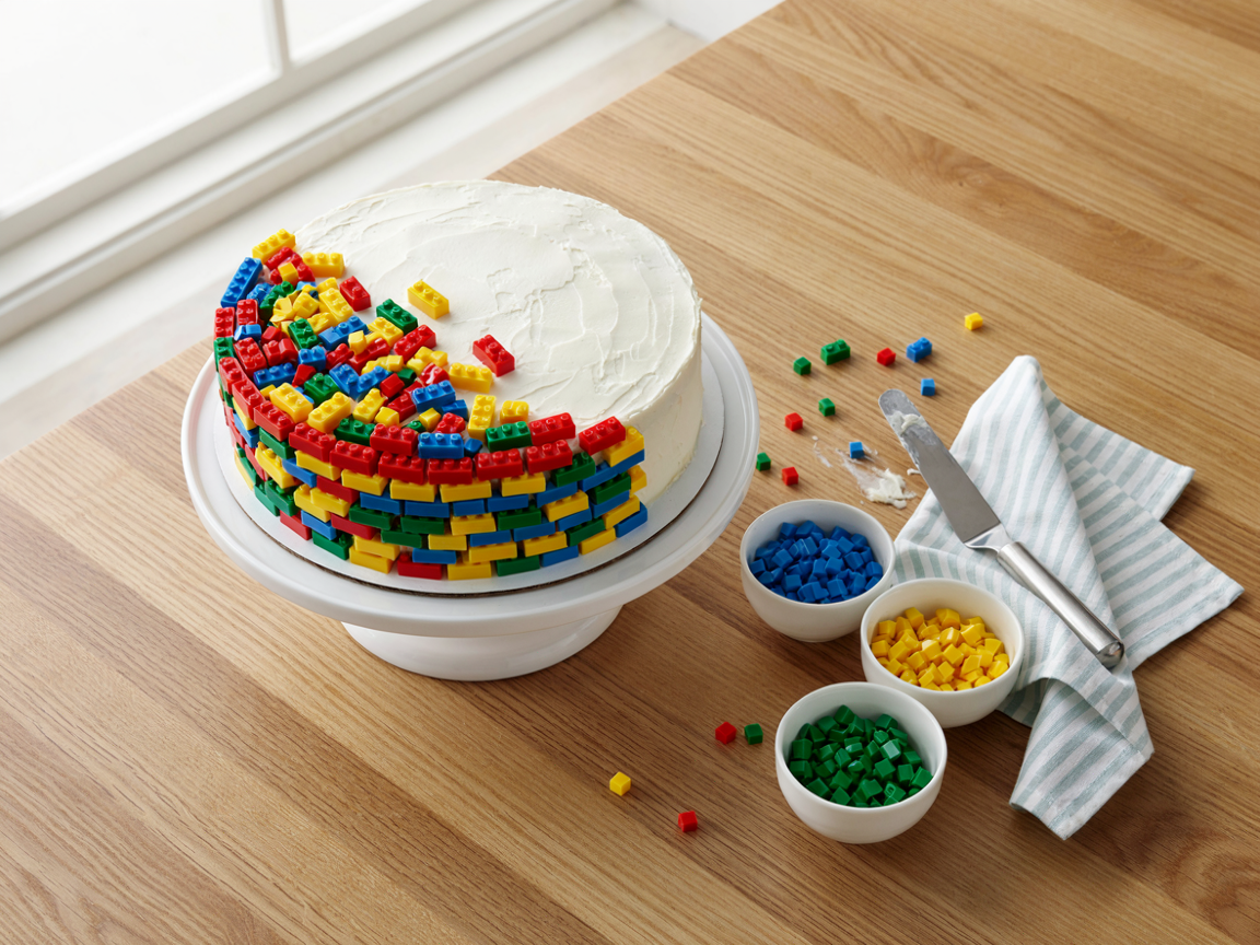 Plain white cake half decorated with candy bricks, with bowls of bricks around it